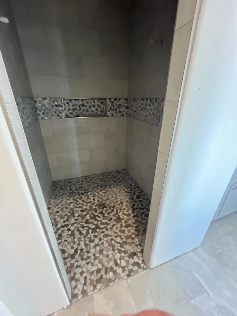 Walk-in shower with pebble mosaic floor, wall tile, and decorative pebble accent band